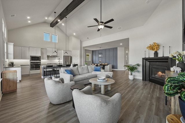 1715 Holly Oak Way, Fate, TX 75087 - living area with high vaulted ceiling, beam ceiling, ceiling fan, dark wood finished floors, and a glass covered fireplace