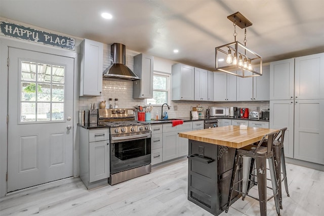 7063 Dover Ln, Richland Hills, TX 76118 - kitchen with stainless steel gas range, wall chimney range hood, wooden counters, white microwave, and decorative backsplash