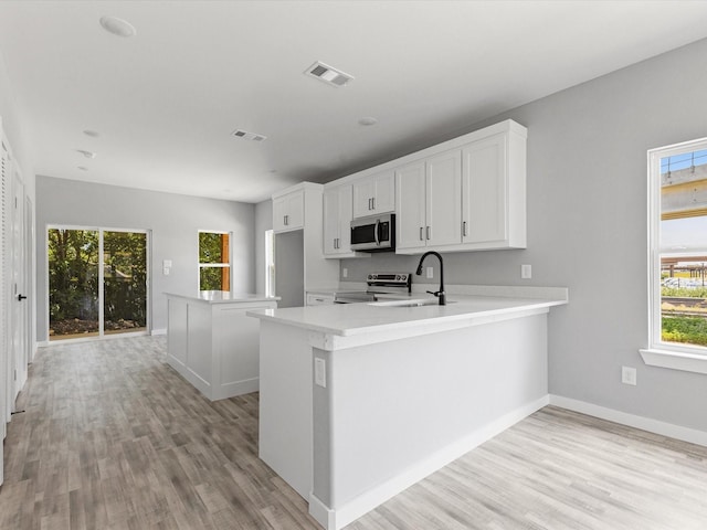 1609 E Bluff St, Fort Worth, TX 76102 - kitchen with stainless steel appliances, light wood-type flooring, light countertops, white cabinets, and a peninsula