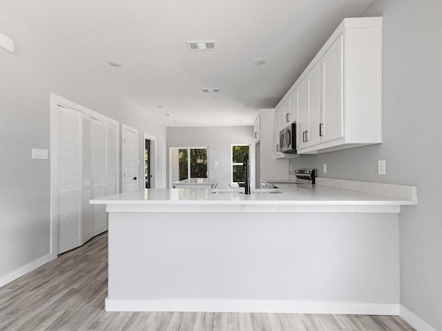 1609 E Bluff St, Fort Worth, TX 76102 - kitchen with stainless steel appliances, light countertops, a peninsula, light wood-style floors, and white cabinets