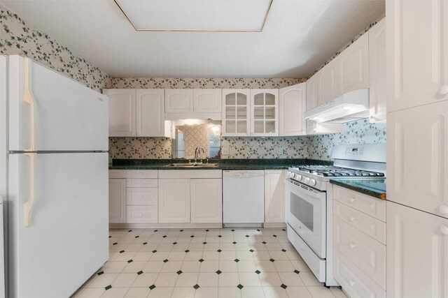 3808 Leland Ave, Waco, TX 76708 - kitchen featuring white appliances, glass insert cabinets, dark countertops, wallpapered walls, and white cabinets
