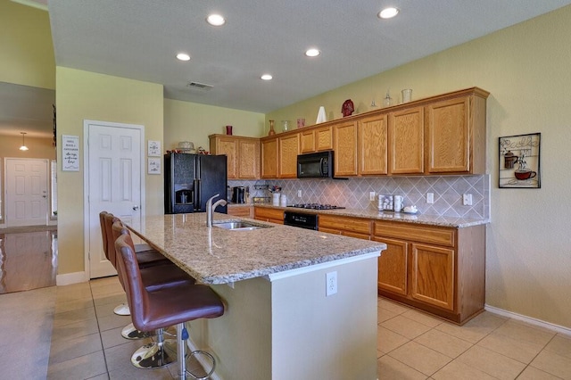 1013 Lilac Ln, Desoto, TX 75115 - kitchen featuring black appliances, light tile patterned floors, an island with sink, decorative backsplash, and light stone counters