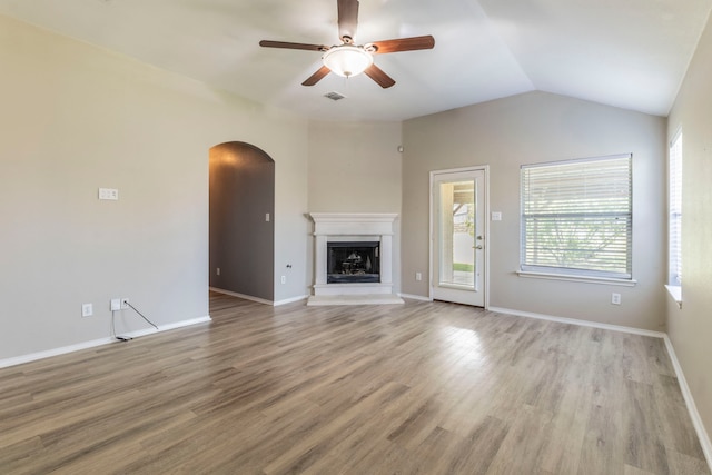 8128 Guadalupe Rd, Arlington, TX 76002 - unfurnished living room featuring arched walkways, ceiling fan, light wood-style floors, a fireplace with raised hearth, and lofted ceiling