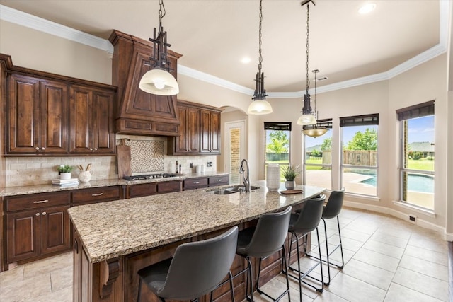 18044 Langford Ln, Talty, TX 75126 - kitchen with decorative backsplash, an island with sink, ornamental molding, light tile patterned floors, and light stone countertops