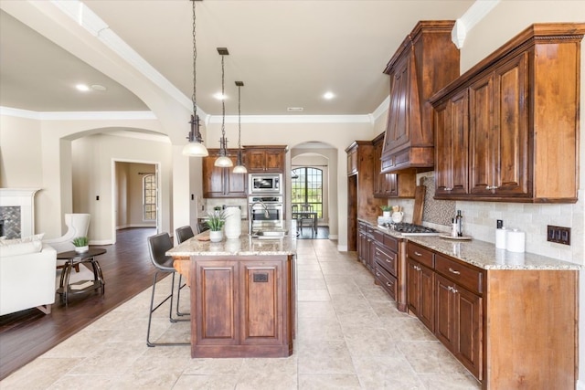 18044 Langford Ln, Talty, TX 75126 - kitchen featuring arched walkways, stainless steel appliances, a kitchen breakfast bar, crown molding, and light stone counters