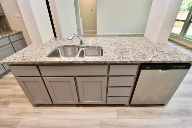 2605 Donella Dr, Denton, TX 76207 - kitchen with gray cabinetry, stainless steel dishwasher, light wood-type flooring, light stone counters, and a center island with sink