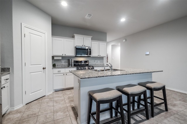 632 Peshtigo Rd, Justin, TX 76247 - kitchen with appliances with stainless steel finishes, an island with sink, a kitchen bar, white cabinetry, and light stone counters