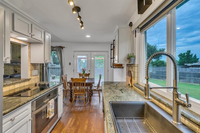 1737 Live Oak Ct, Lewisville, TX 75067 - kitchen with oven, black electric cooktop, dark wood-style flooring, tasteful backsplash, and light stone countertops