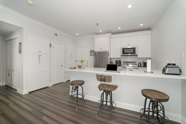 3400 Welborn St Unit 224, Dallas, TX 75219 - kitchen with appliances with stainless steel finishes, a breakfast bar, white cabinetry, dark wood-style flooring, and crown molding