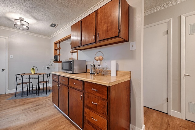 531 Himes Dr, Euless, TX 76039 - kitchen featuring stainless steel microwave, light wood-style flooring, a textured ceiling, light countertops, and crown molding