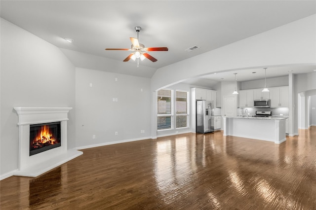 5608 Grove Cove Dr, Mckinney, TX 75071 - unfurnished living room featuring a glass covered fireplace, wood finished floors, a ceiling fan, vaulted ceiling, and arched walkways