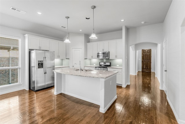 5608 Grove Cove Dr, Mckinney, TX 75071 - kitchen with stainless steel appliances, arched walkways, backsplash, a kitchen island with sink, and white cabinets