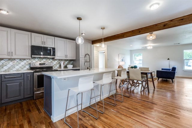 10649 Sylvia Dr, Dallas, TX 75228 - kitchen featuring appliances with stainless steel finishes, wood finished floors, light countertops, tasteful backsplash, and a kitchen breakfast bar
