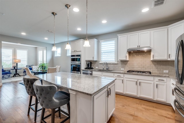2129 Harbor Pointe Dr, Frisco, TX 75036 - kitchen with under cabinet range hood, appliances with stainless steel finishes, a kitchen island, tasteful backsplash, and white cabinetry