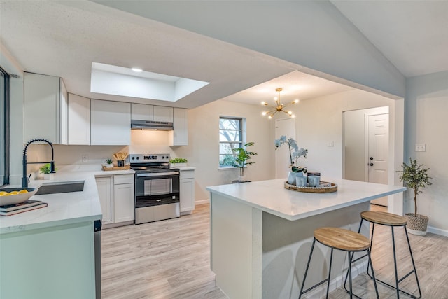 409 Brookview Dr, Garland, TX 75043 - kitchen with stainless steel range with electric stovetop, under cabinet range hood, light wood-style floors, a kitchen bar, and a center island