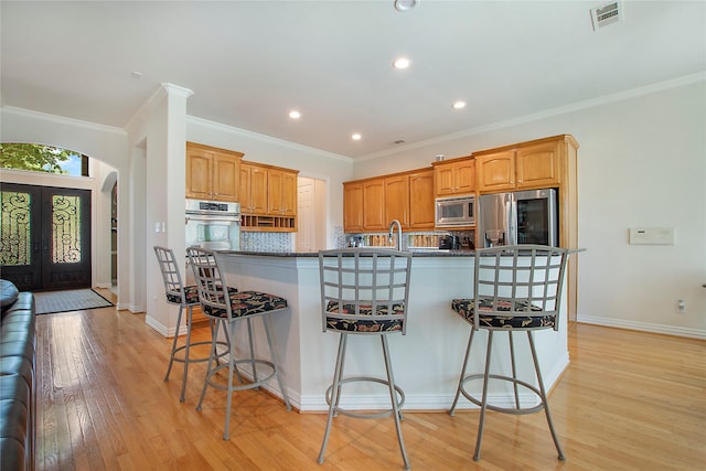 2327 Clearspring Dr N, Irving, TX 75063 - kitchen featuring stainless steel appliances, a kitchen bar, light wood-style floors, a center island with sink, and arched walkways