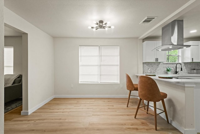 709 E Gandy St, Denison, TX 75021 - kitchen with island exhaust hood, light countertops, a breakfast bar, a chandelier, and light wood-type flooring