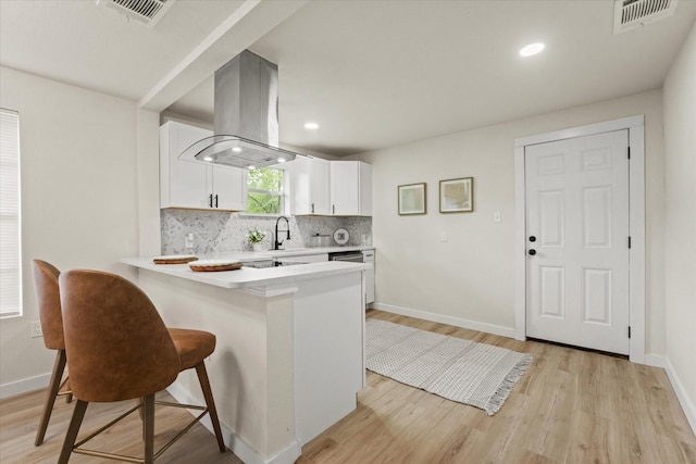 709 E Gandy St, Denison, TX 75021 - kitchen featuring island range hood, light countertops, light wood finished floors, backsplash, and white cabinetry