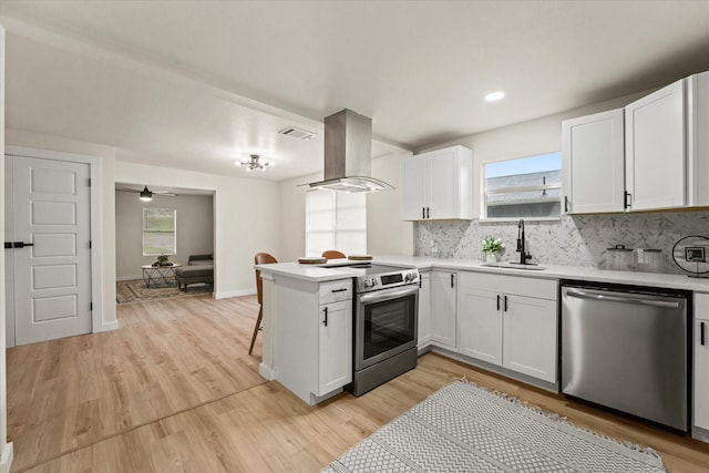 709 E Gandy St, Denison, TX 75021 - kitchen featuring appliances with stainless steel finishes, island range hood, a peninsula, light countertops, and white cabinets