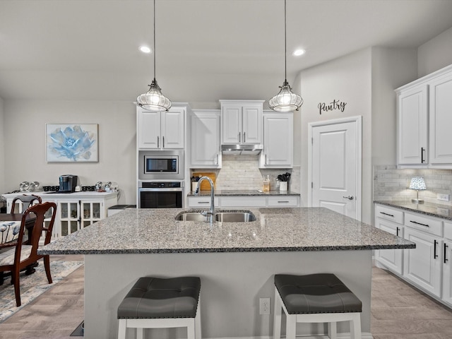 5622 Log Cabin Ct, Midlothian, TX 76065 - kitchen with appliances with stainless steel finishes, under cabinet range hood, a kitchen breakfast bar, stone countertops, and recessed lighting