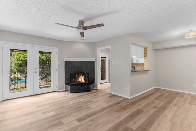 333 Melrose Dr Unit 4D, Richardson, TX 75080 - unfurnished living room with light wood-style flooring, a ceiling fan, a textured ceiling, a tiled fireplace, and french doors