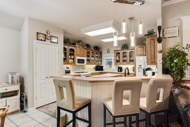 3001 Coventry Ln, Waxahachie, TX 75165 - kitchen featuring white appliances, a peninsula, light tile patterned floors, a breakfast bar area, and brown cabinetry