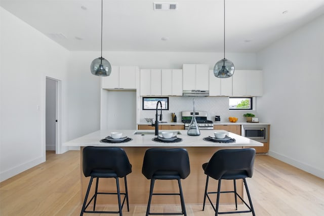 430 E 8th Unit 101, Dallas, TX 75203 - kitchen with stainless steel appliances, white cabinets, light countertops, light wood-type flooring, and a kitchen bar