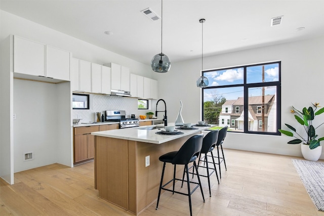 430 E 8th Unit 101, Dallas, TX 75203 - kitchen with gas stove, light wood finished floors, under cabinet range hood, a kitchen island with sink, and white cabinetry
