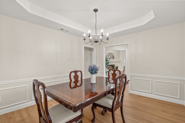 2305 Delmar Dr, Plano, TX 75075 - dining space featuring a chandelier, a raised ceiling, light wood finished floors, wainscoting, and a decorative wall