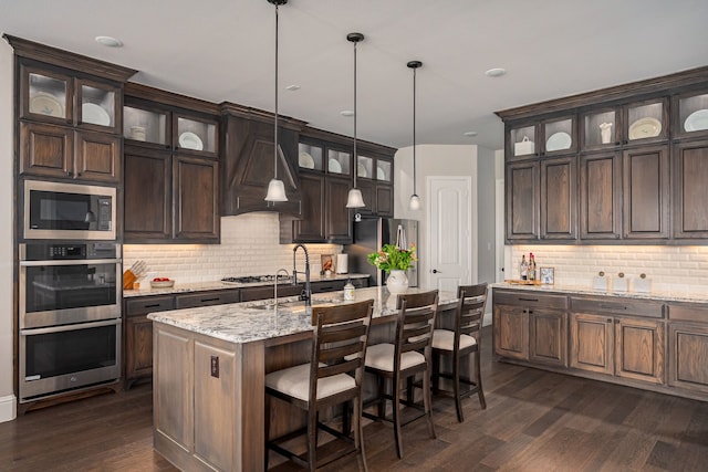 1251 Castle Dr, Prosper, TX 75078 - kitchen featuring stainless steel appliances, backsplash, dark wood-style floors, dark brown cabinetry, and a kitchen island with sink