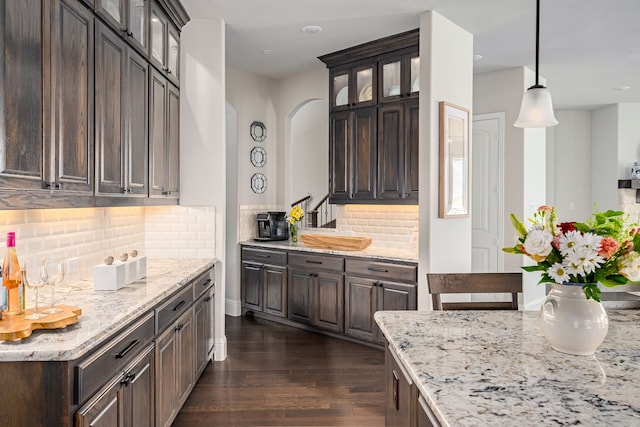 1251 Castle Dr, Prosper, TX 75078 - kitchen featuring dark brown cabinets, dark wood-style floors, backsplash, glass insert cabinets, and light stone counters