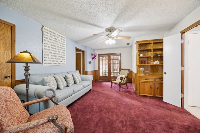 1301 Warwick St, Garland, TX 75040 - carpeted living room with ceiling fan, a textured ceiling, a wainscoted wall, french doors, and wood walls