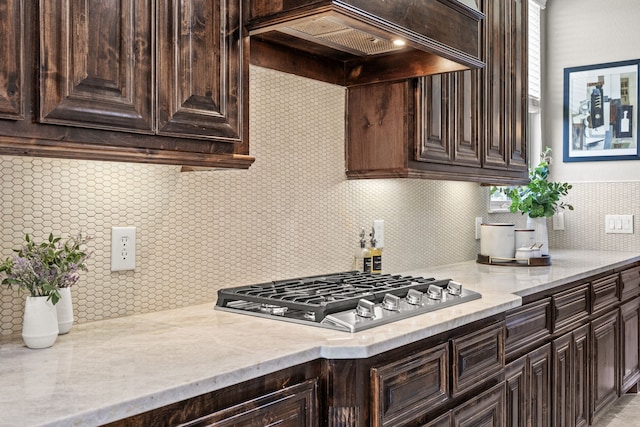 881 Derick Ln, Prosper, TX 75078 - kitchen featuring stainless steel gas stovetop, custom range hood, dark brown cabinets, backsplash, and light stone countertops