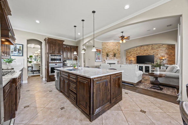 881 Derick Ln, Prosper, TX 75078 - kitchen with arched walkways, ceiling fan, stainless steel appliances, dark brown cabinetry, and light stone counters