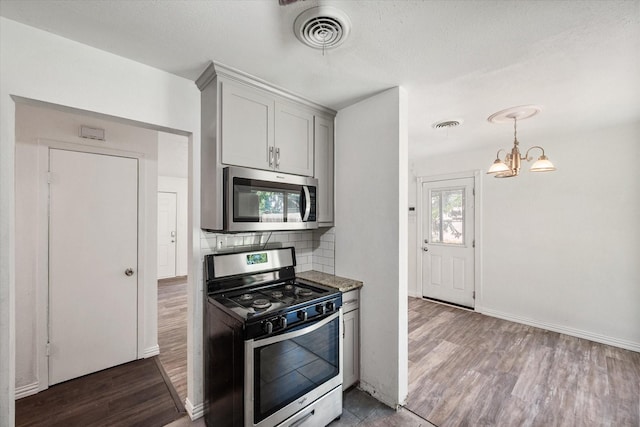 612 Elm St, Hurst, TX 76053 - kitchen with appliances with stainless steel finishes, wood finished floors, a chandelier, and decorative backsplash