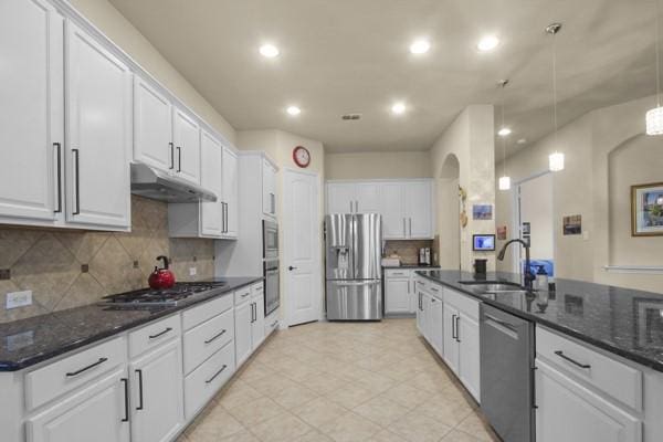 1165 Breakwater Dr, Frisco, TX 75036 - kitchen featuring appliances with stainless steel finishes, white cabinetry, under cabinet range hood, arched walkways, and decorative backsplash