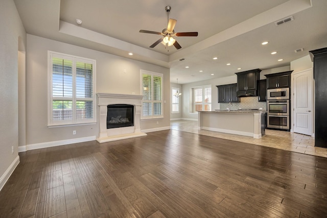 15005 Teasley Ave, Aledo, TX 76008 - unfurnished living room featuring a tray ceiling, a ceiling fan, a glass covered fireplace, light wood-style flooring, and recessed lighting