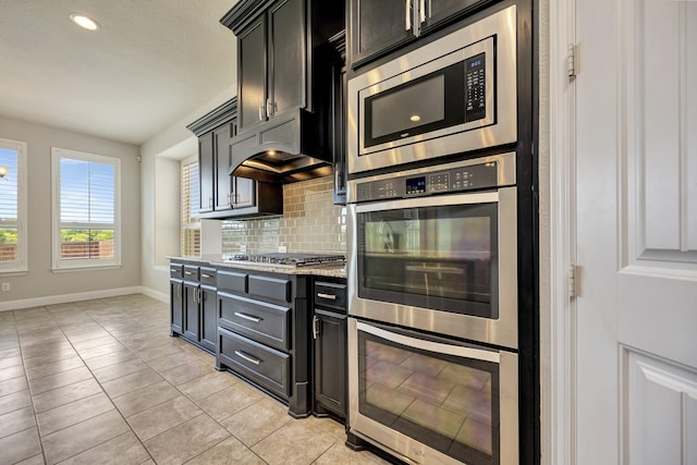 15005 Teasley Ave, Aledo, TX 76008 - kitchen featuring appliances with stainless steel finishes, tasteful backsplash, light tile patterned floors, dark cabinets, and recessed lighting