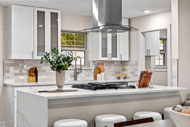 10017 Lanshire Dr, Dallas, TX 75238 - kitchen featuring island exhaust hood, backsplash, white cabinets, a kitchen bar, and stainless steel gas cooktop