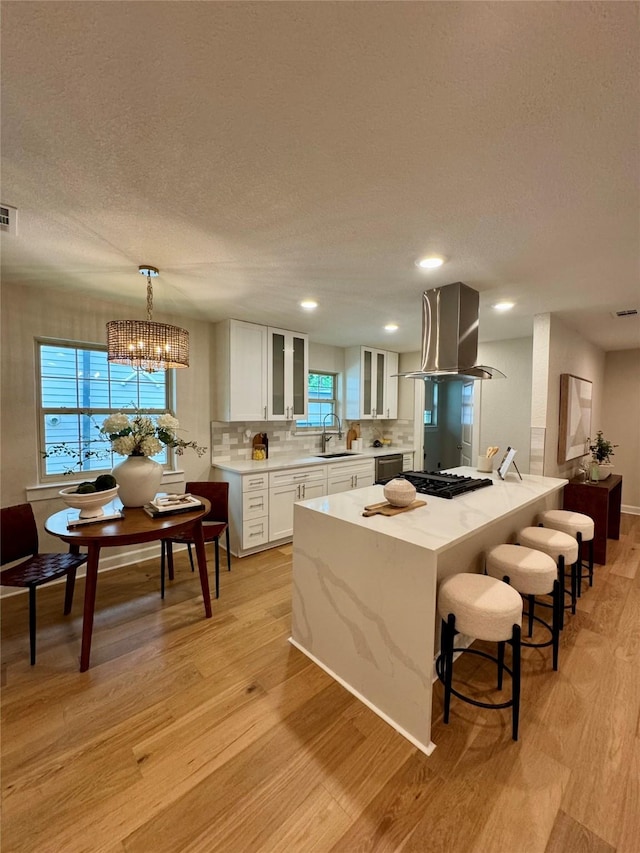 10017 Lanshire Dr, Dallas, TX 75238 - kitchen with island exhaust hood, light wood-style floors, white cabinetry, glass insert cabinets, and a textured ceiling