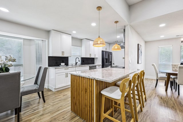 1722 Brighton Dr, Carrollton, TX 75007 - kitchen featuring refrigerator with ice dispenser, light wood-type flooring, light stone countertops, white cabinetry, and a kitchen bar