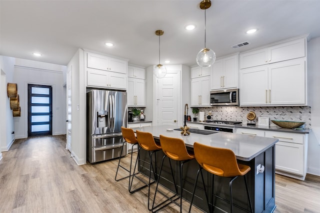 2413 Latimer Mews, Celina, TX 75009 - kitchen with stainless steel appliances, backsplash, a breakfast bar area, light wood-type flooring, and a center island with sink