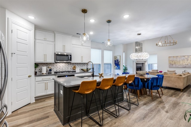 2413 Latimer Mews, Celina, TX 75009 - kitchen featuring stainless steel microwave, a kitchen breakfast bar, decorative backsplash, light wood finished floors, and a center island with sink