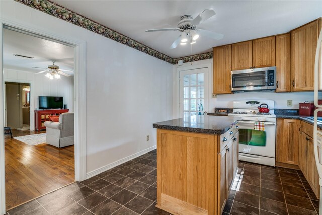 1312 Linden Ln, Garland, TX 75040 - kitchen featuring white range with gas stovetop, stainless steel microwave, a ceiling fan, dark tile patterned floors, and a kitchen island