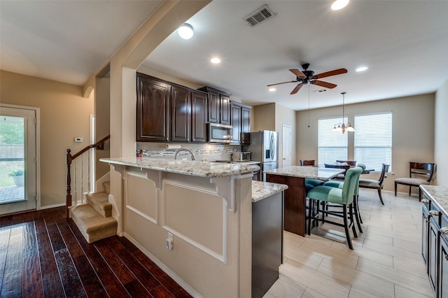 2748 Indian Oak Dr, Mckinney, TX 75071 - kitchen featuring appliances with stainless steel finishes, a kitchen island, a breakfast bar, ceiling fan, and dark brown cabinetry