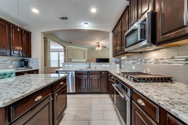 2748 Indian Oak Dr, Mckinney, TX 75071 - kitchen with stainless steel appliances, ceiling fan, arched walkways, ornate columns, and backsplash