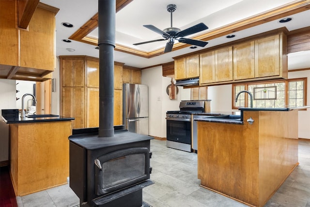 1933 E Hickory Hill Rd, Argyle, TX 76226 - kitchen featuring appliances with stainless steel finishes, a tray ceiling, brown cabinetry, a wood stove, and dark countertops