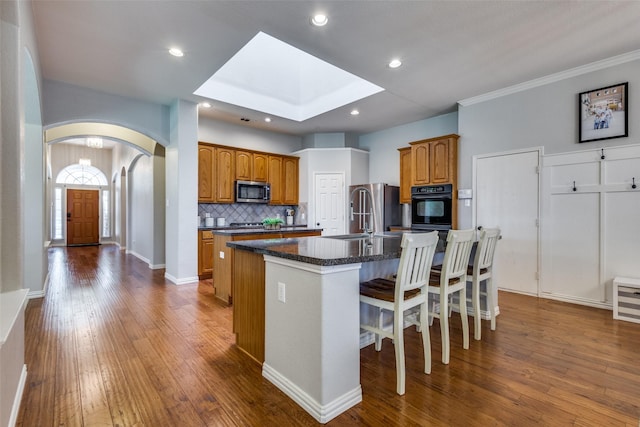 5628 Vineyard Ln, Mckinney, TX 75070 - kitchen with a kitchen island with sink, arched walkways, tasteful backsplash, dark wood-style flooring, and brown cabinetry