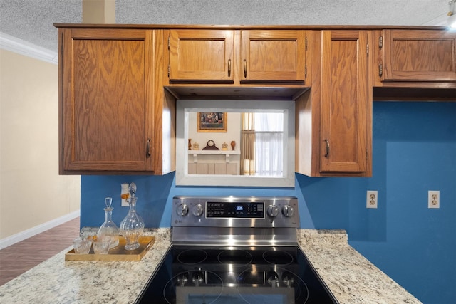 6503 Ridgecrest Rd Unit 107G, Dallas, TX 75231 - kitchen with stainless steel range with electric stovetop, ornamental molding, wood finished floors, brown cabinetry, and light stone countertops