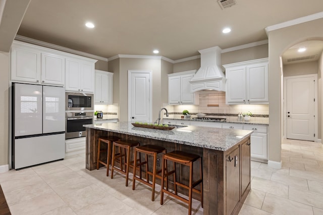 8240 Odell St, North Richland Hills, TX 76182 - kitchen with appliances with stainless steel finishes, premium range hood, tasteful backsplash, white cabinetry, and a breakfast bar